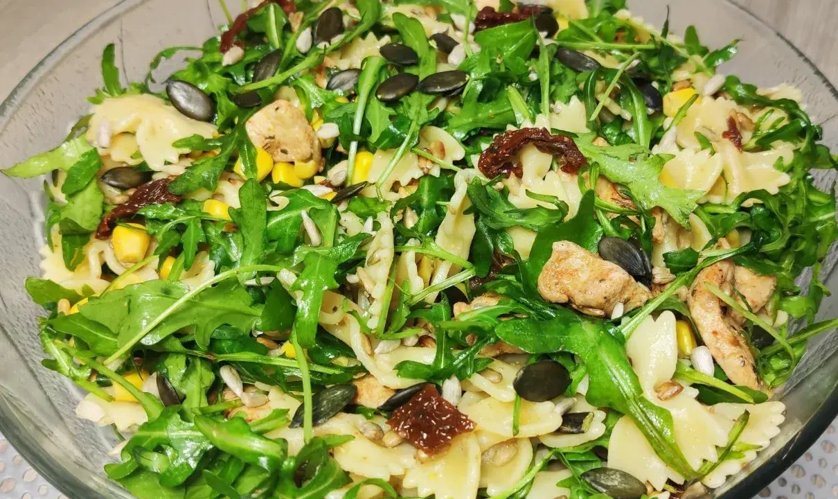 Kolorowa sałatka z makaronem farfalle, rukolą, kurczakiem, kukurydzą i słonecznikiem, wzbogacona o intensywny smak suszonych pomidorów.