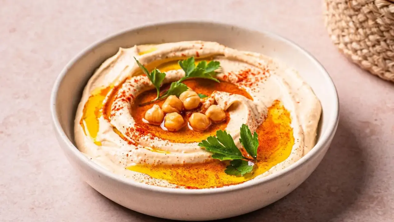 Cremiger Hummus in einer Schüssel, garniert mit Kichererbsen, Petersilie und Paprikapulver. Ein köstliches Gericht mit Hummus, bereit zum Genießen.