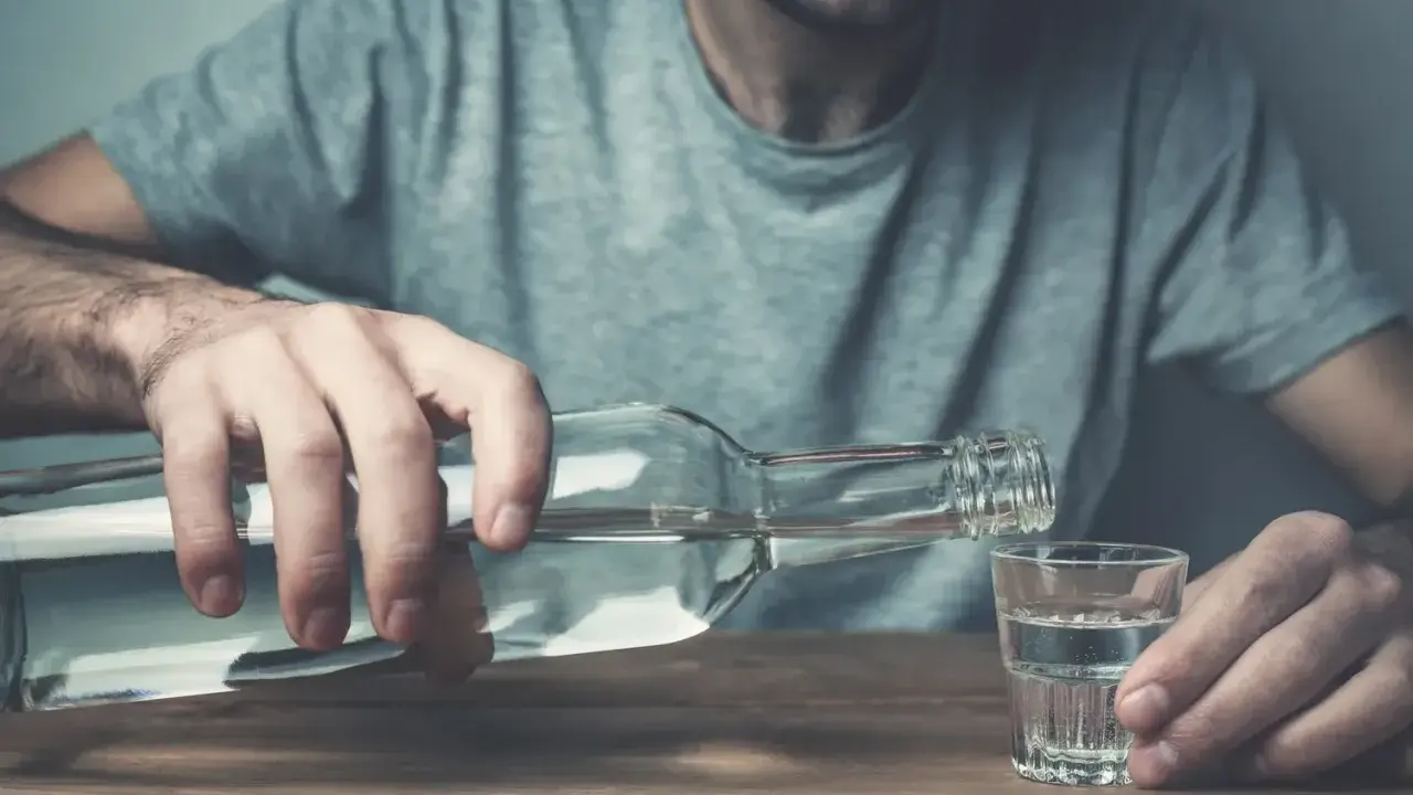 Mężczyzna nalewa alkohol do kieliszka. Czy wszywka jest skuteczna w walce z nałogiem?