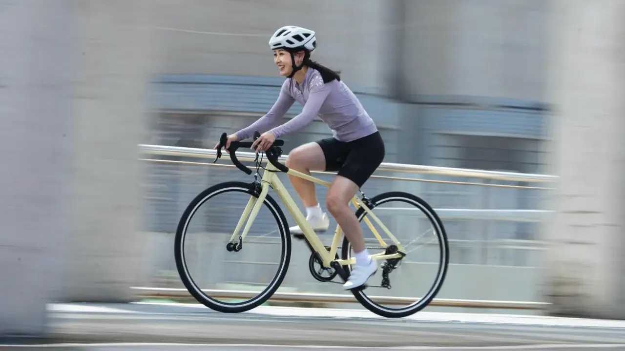 Uśmiechnięta kobieta w kasku pędzi na rowerze, ciesząc się sportami rowerowymi.