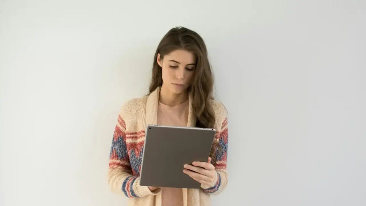Kobieta w swetrze z wzorem przegląda tablet, być może szukając informacji o długoterminowym zwolnieniu lekarskim.