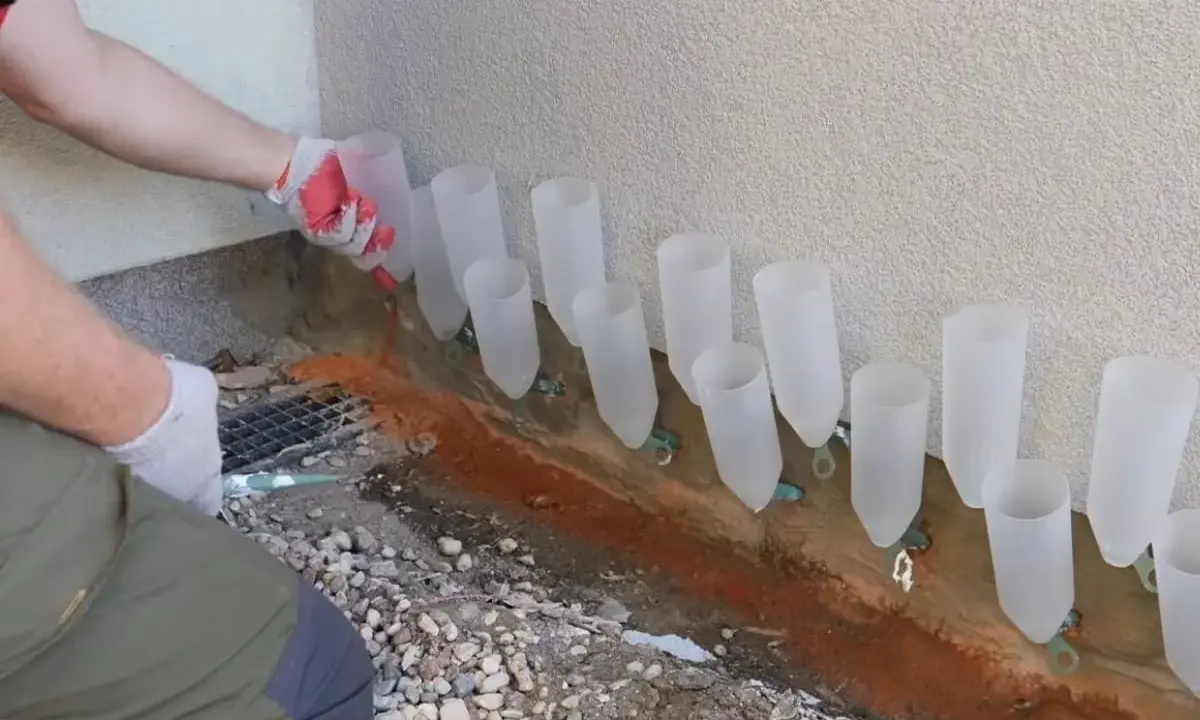 Osoba w rękawiczkach ustawia rurki przy ścianie, pokazując, jak osuszyć ściany domowym sposobem.