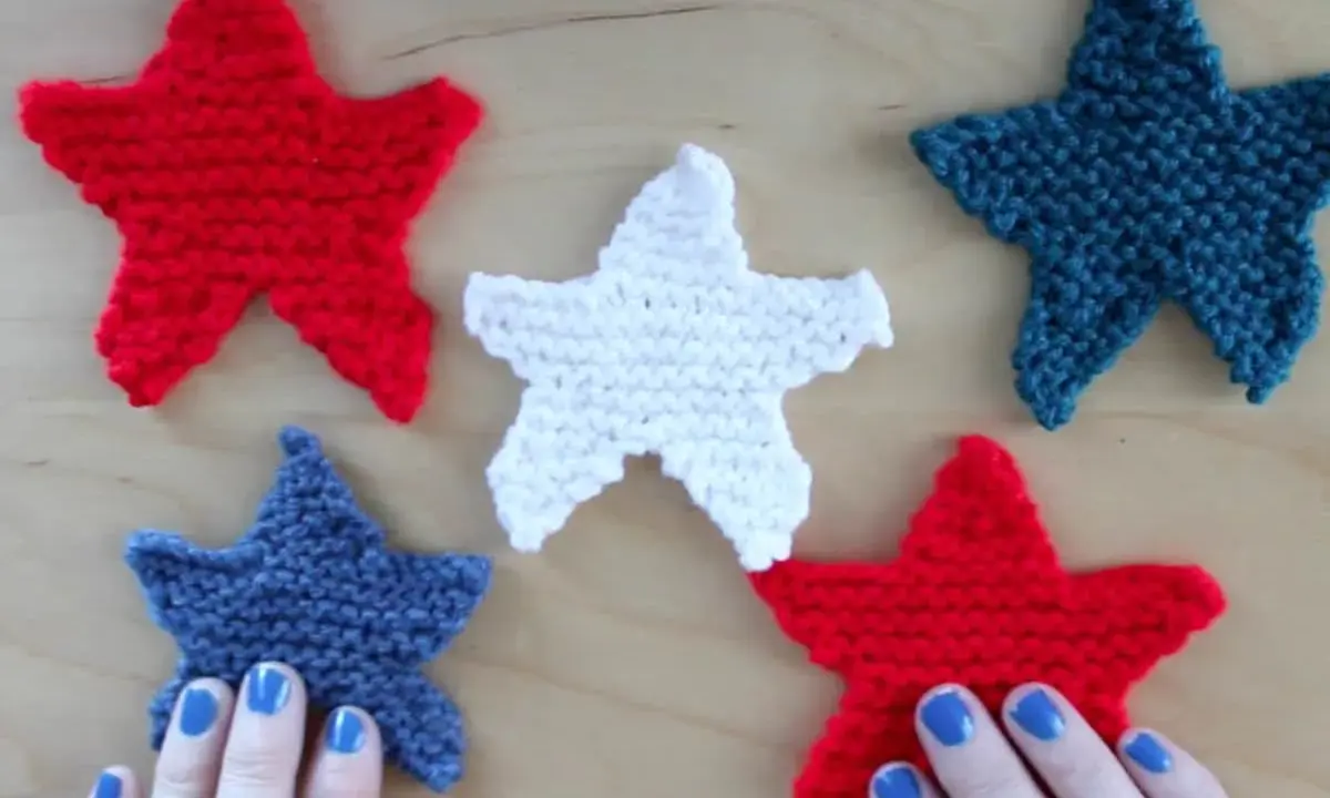 Cinco estrellas tejidas de punto estrella, rojas, blancas y azules, dispuestas sobre una superficie de madera.