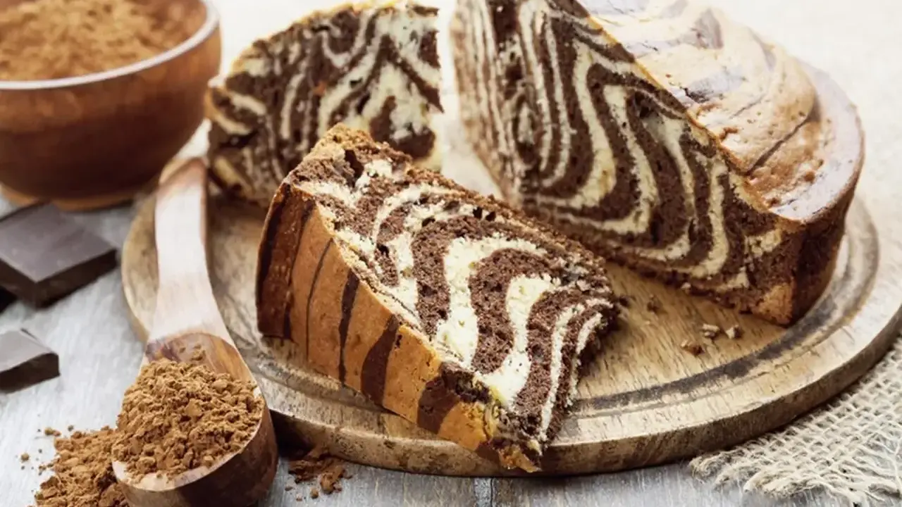 Wilgotne ciasto zebra z czekoladowymi i waniliowymi pasami, pokrojone na plastry, obok kakao i czekolady.