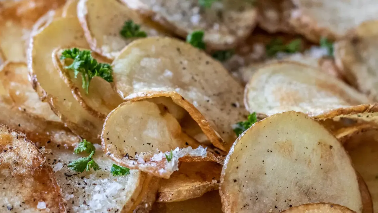 Krispiga, gyllene skivor av friterad potatis, strödda med salt och peppar, toppade med färsk persilja.