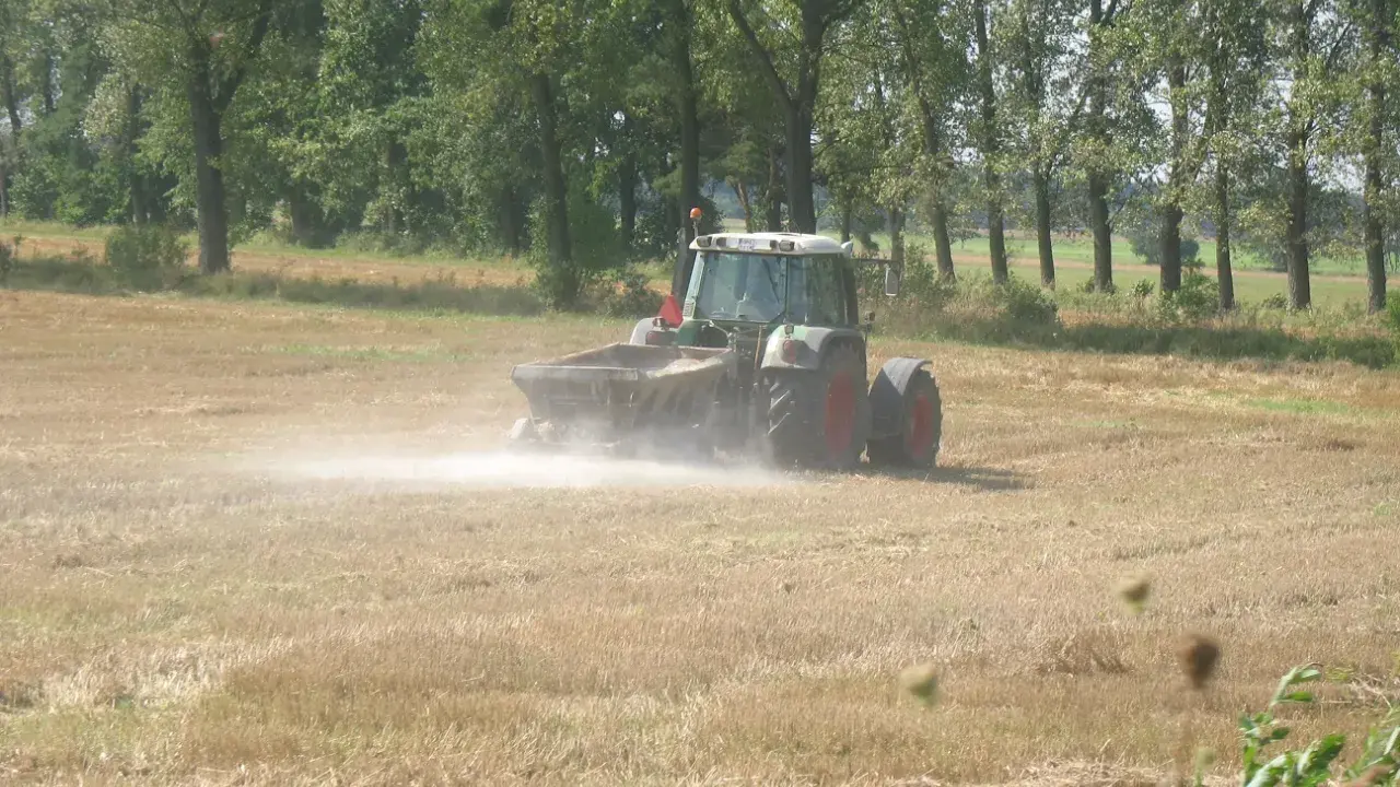 Traktor rozsypuje wapno na polu, pokazując, co daje wapnowanie gleby. Poprawia jej strukturę i żyzność.