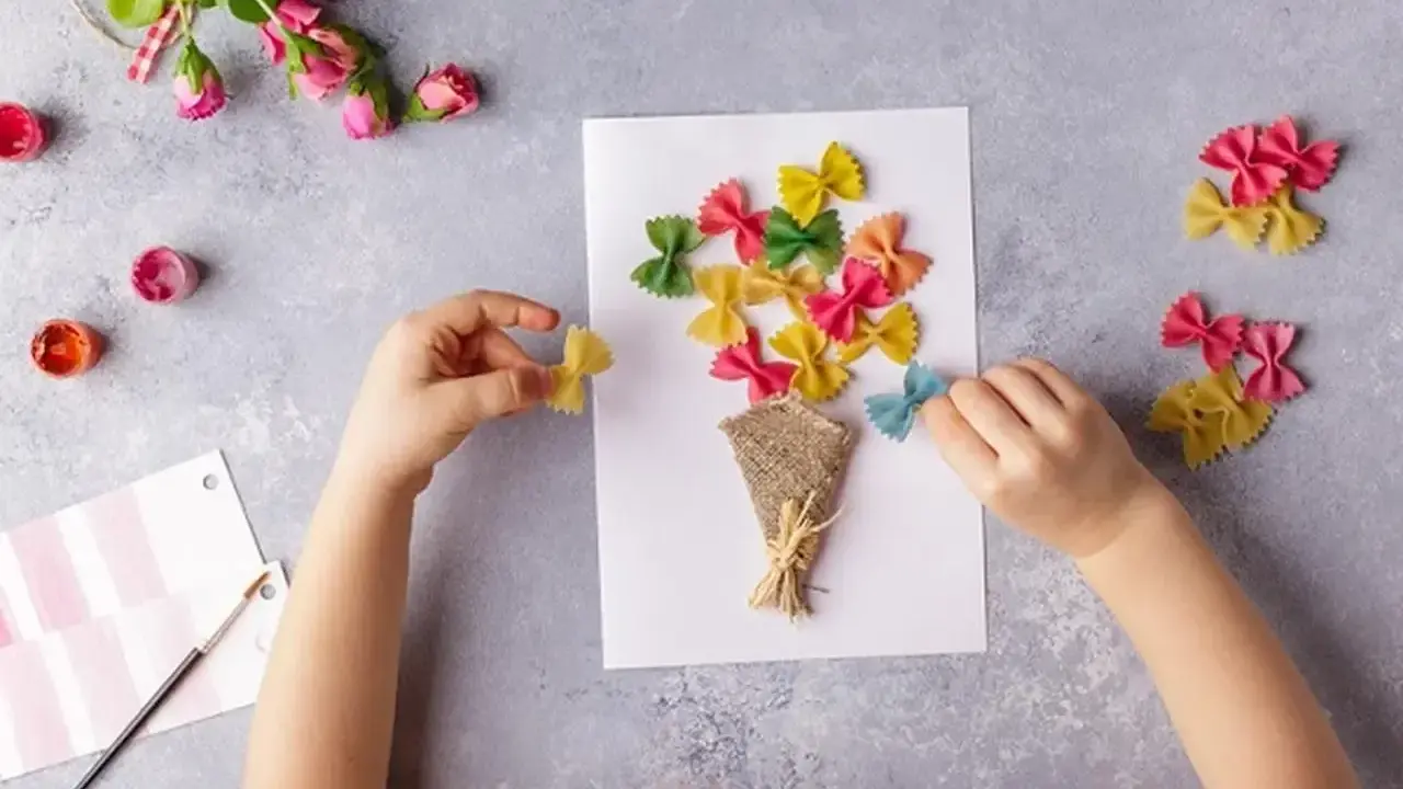 Dziecko tworzy bukiet z kolorowego makaronu farfalle na laurce. Świetne pomysły na laurki!