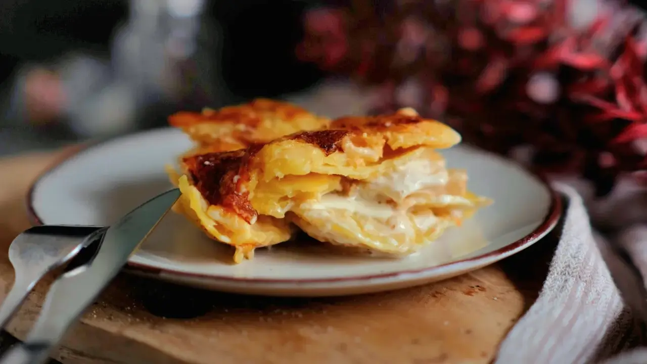 Ein Stück cremiges Kartoffelgratin mit goldbrauner Kruste auf einem Teller, bereit zum Servieren. Dieses Kartoffelgratin Rezept ist ein Genuss!