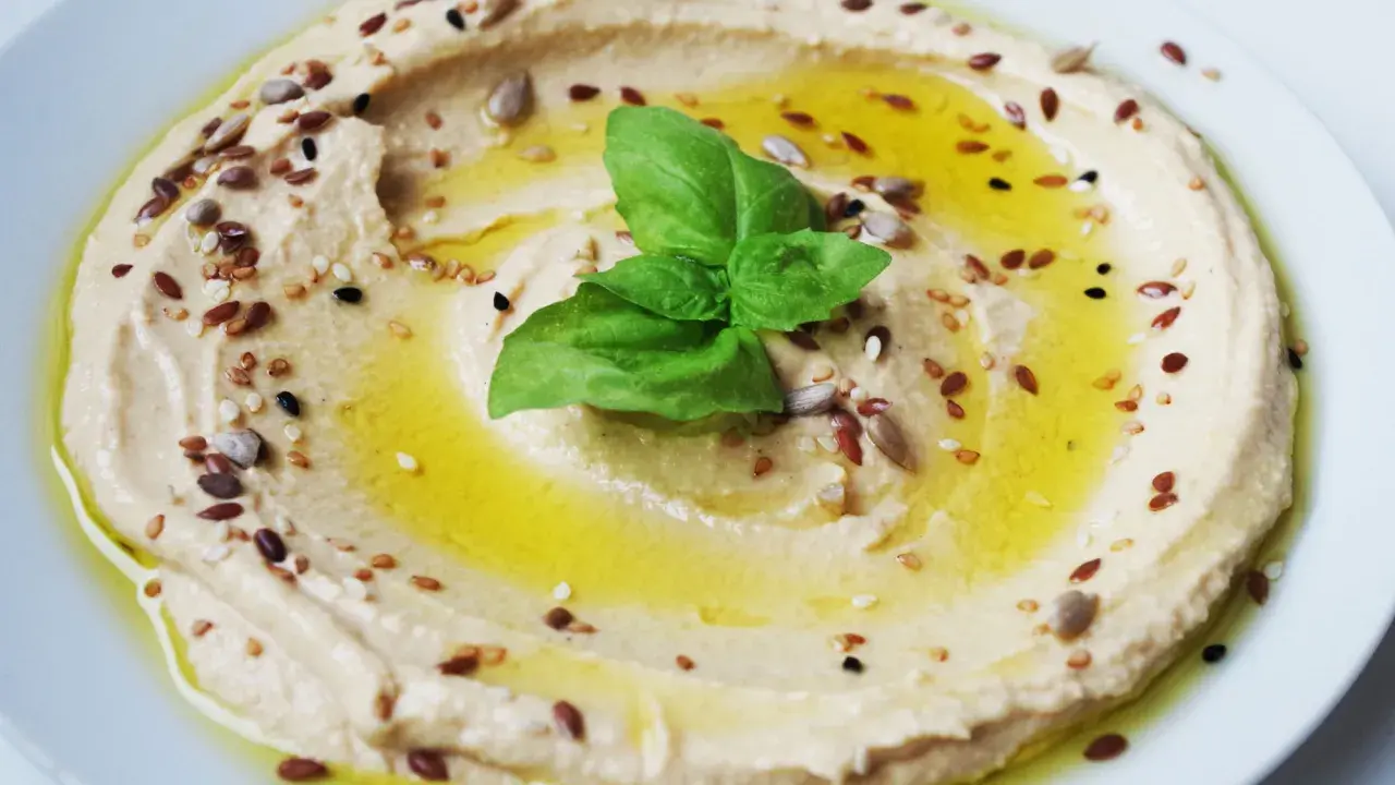 Cremiger Hummus, garniert mit Öl, Kräutern und Samen. Tahin ist die geheime Zutat für diese köstliche Dip-Kreation.