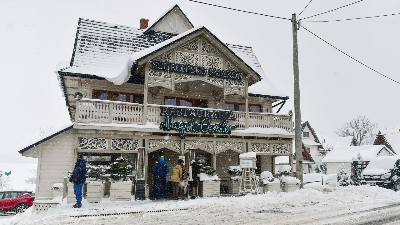 Drewniana chata z napisem "Schronisko Smaków" i neonem "Restauracja" w Bukowinie Tatrzańskiej, otoczona śniegiem.