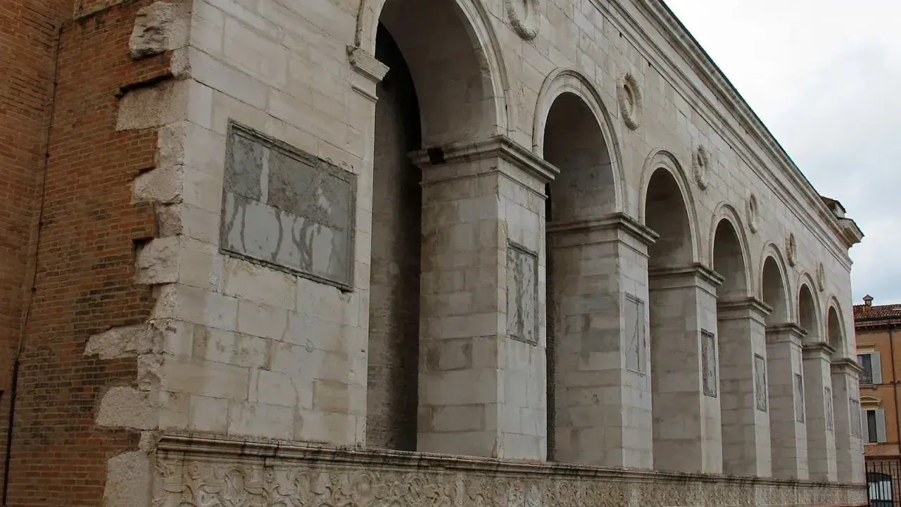 Archi maestosi e decorazioni in pietra della chiesa San Francesco a Rimini, con un muro in mattoni a vista che racconta la sua storia.