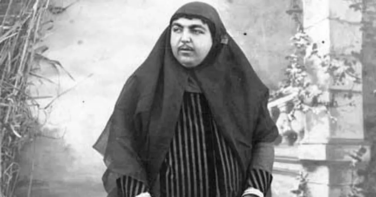 Zahra Khanom Tadj es-Saltaneh, księżniczka perska, w czarnym hidżabie i pasiastym stroju, pozuje na tle ogrodu.