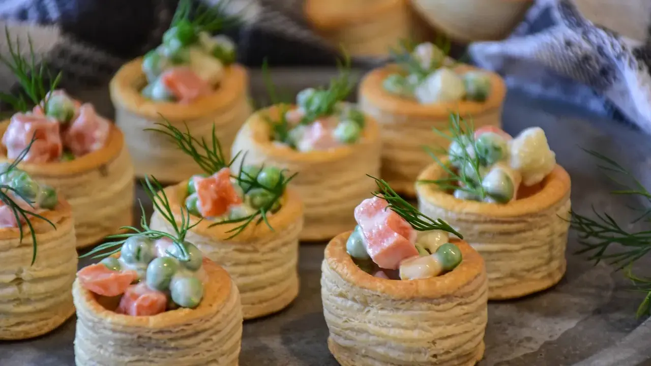 Plusieurs bouchées à la reine garnies d'une salade crémeuse de petits pois, carottes et saumon, décorées d'aneth.