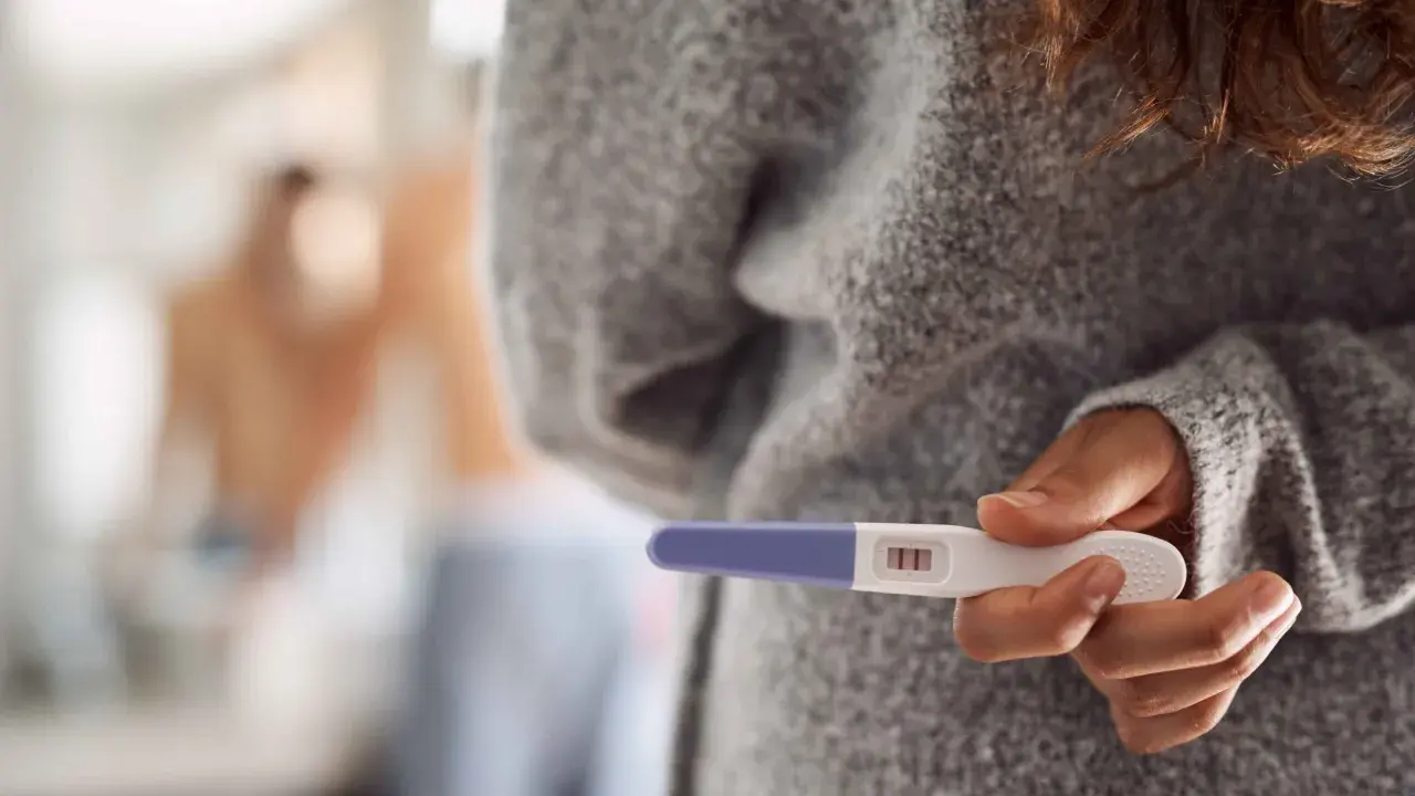 Kobieta trzyma test ciążowy z dwoma kreskami. Czy to oznacza, że dni niepłodne to już przeszłość?