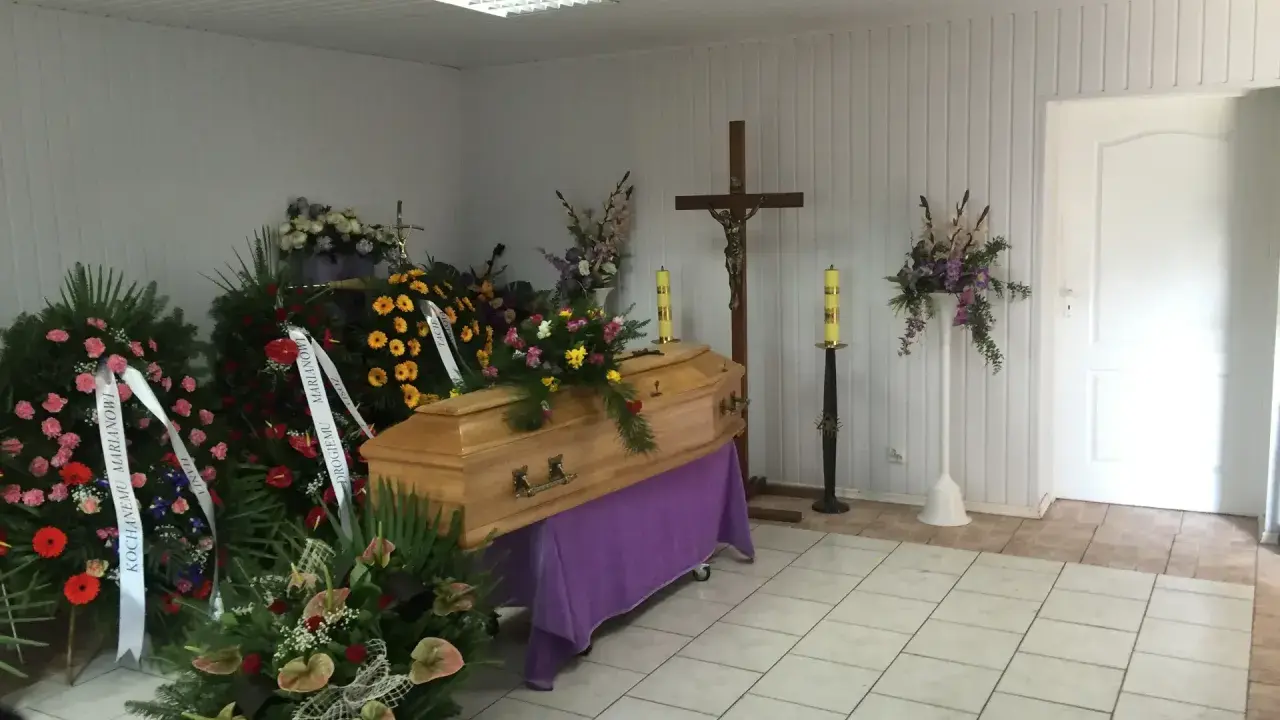 Drewniana trumna otoczona wieńcami i bukietami. Piękne kwiaty na trumnę tworzą smutną, ale uroczystą atmosferę.