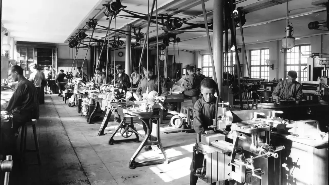 Barn arbetar vid maskiner i en verkstad, en scen från den industriella revolutionen.