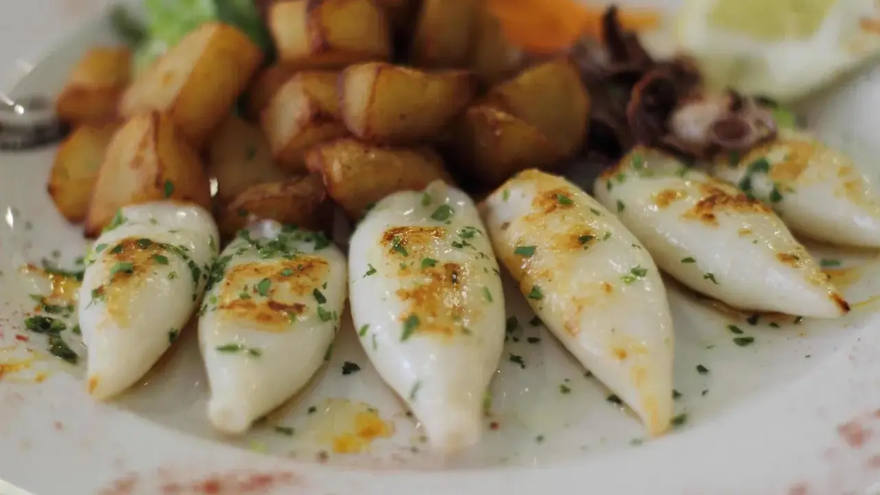 Chipirones a la plancha, tiernos y dorados, acompañados de patatas rústicas y un toque de perejil fresco.