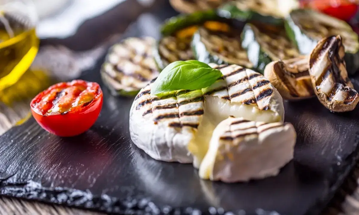Grillowany camembert z pomidorkiem, cukinią i pieczarkami na czarnej desce.