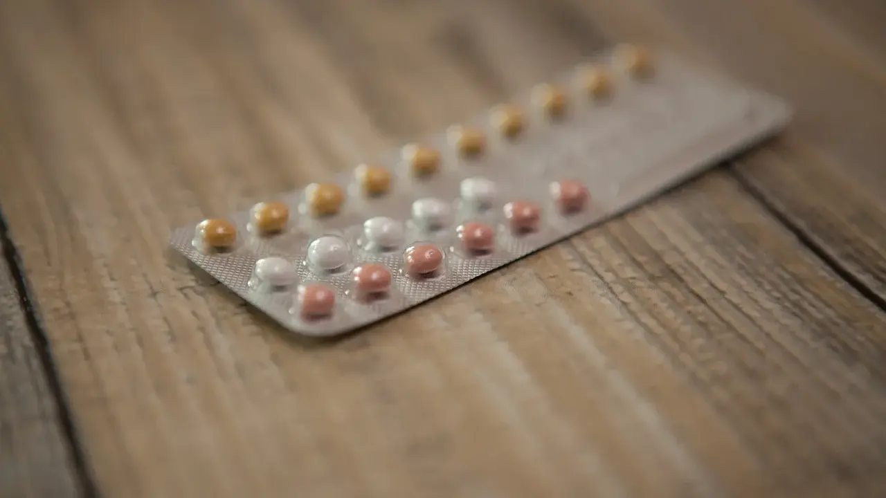 Opakowanie tabletek antykoncepcyjnych z różowymi, białymi i żółtymi pigułkami na drewnianym tle.