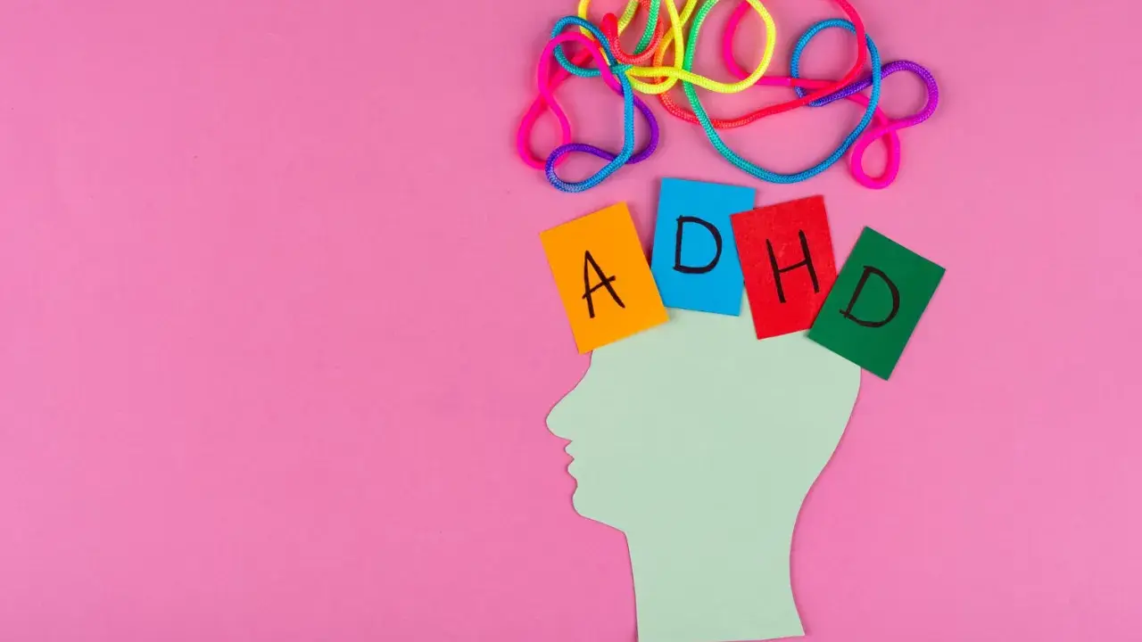 Kolorowe sznurki nad głową symbolizują chaos myśli, jak przy ADHD. Kartki z literami A, D, H, D sugerują trudności w nauce, np. dyskalkulię.