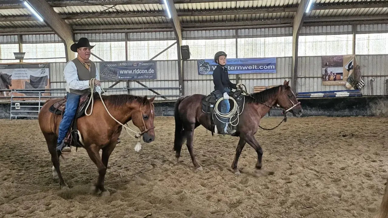 Mann mit Hut und ein Jugendlicher üben Reining Reiten in einer Reithalle.