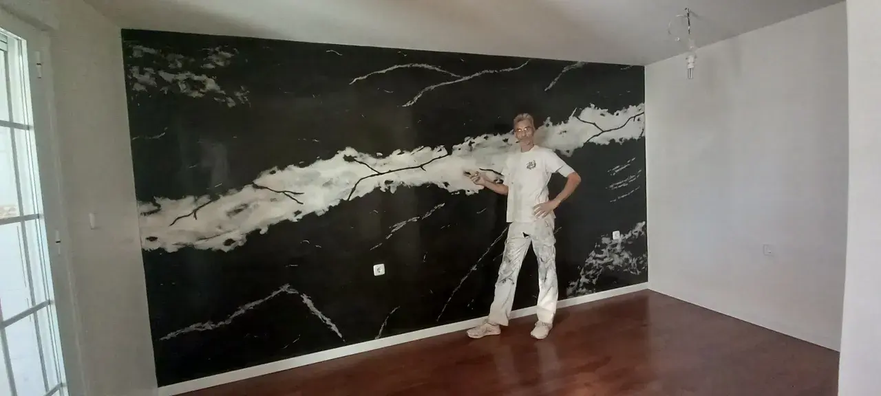 Pintor posa frente a una pared con falso estuco de mármol negro y blanco.