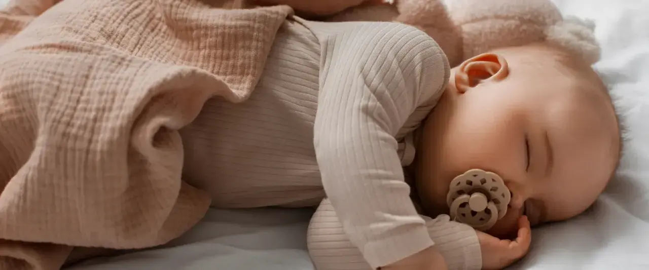Un tenero neonato dorme sereno, avvolto in una copertina color pesca, con un ciuccio che lo culla nel sonno.