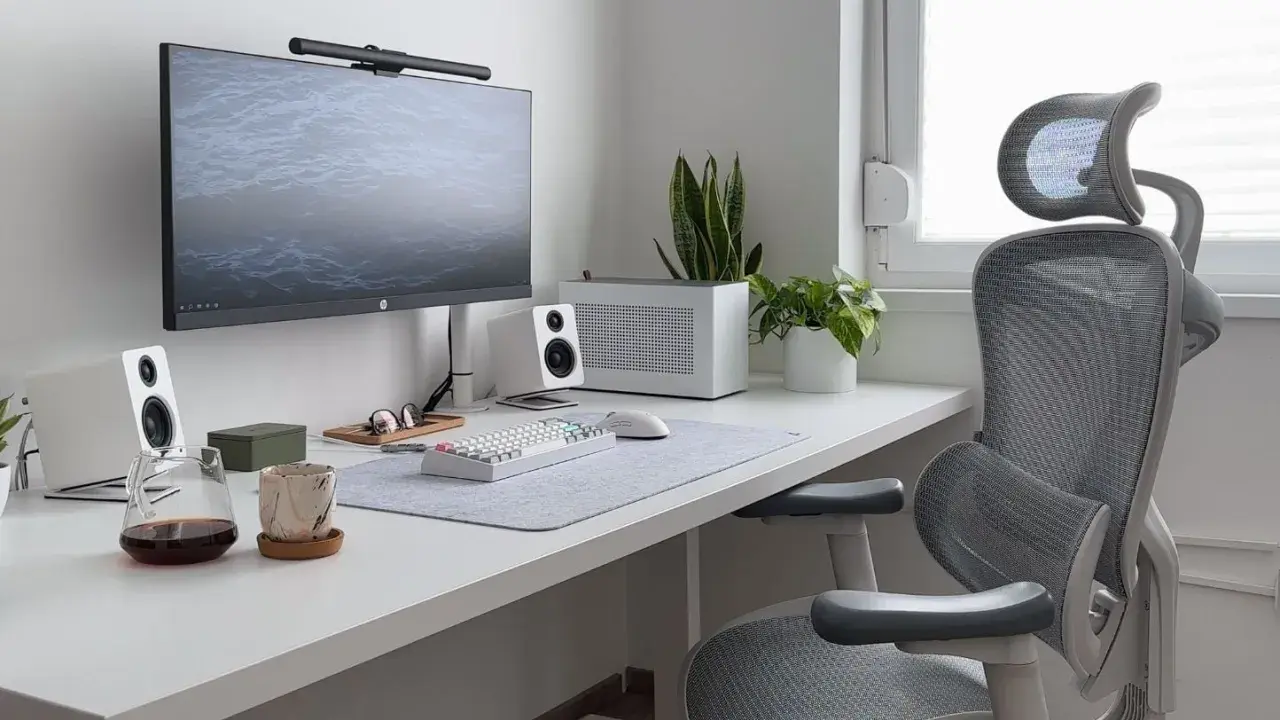 Installation poste de travail épurée avec écran, clavier, souris, enceintes blanches, plantes et chaise ergonomique grise.