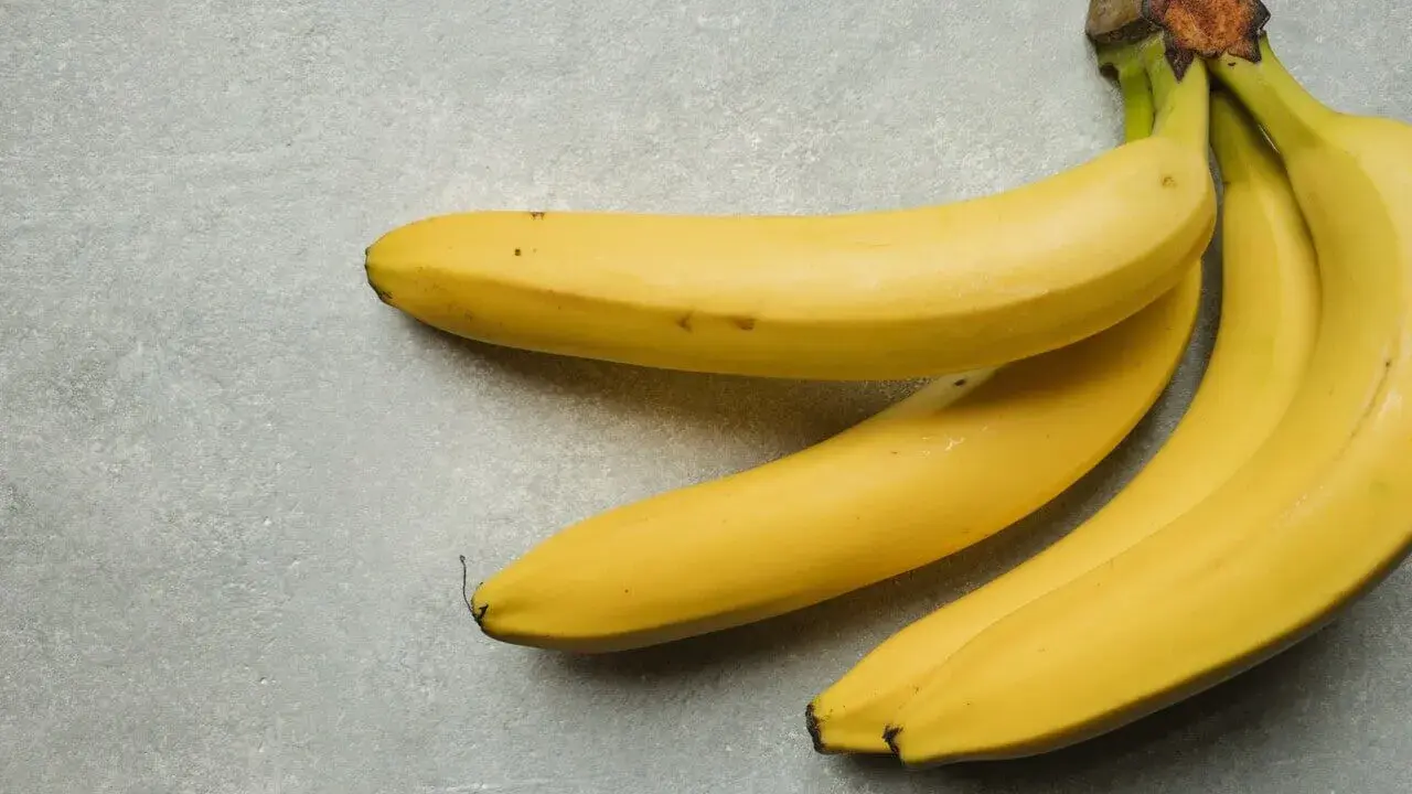 Kilka żółtych bananów leżących na szarym tle.