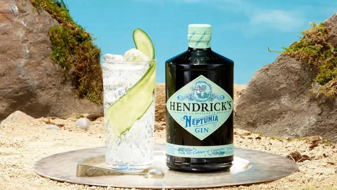 Ein erfrischender Gin Tonic mit Hendricks Neptunia Gin, Gurkenscheiben und Eis, auf sandigem Untergrund mit Felsen und blauem Himmel.
