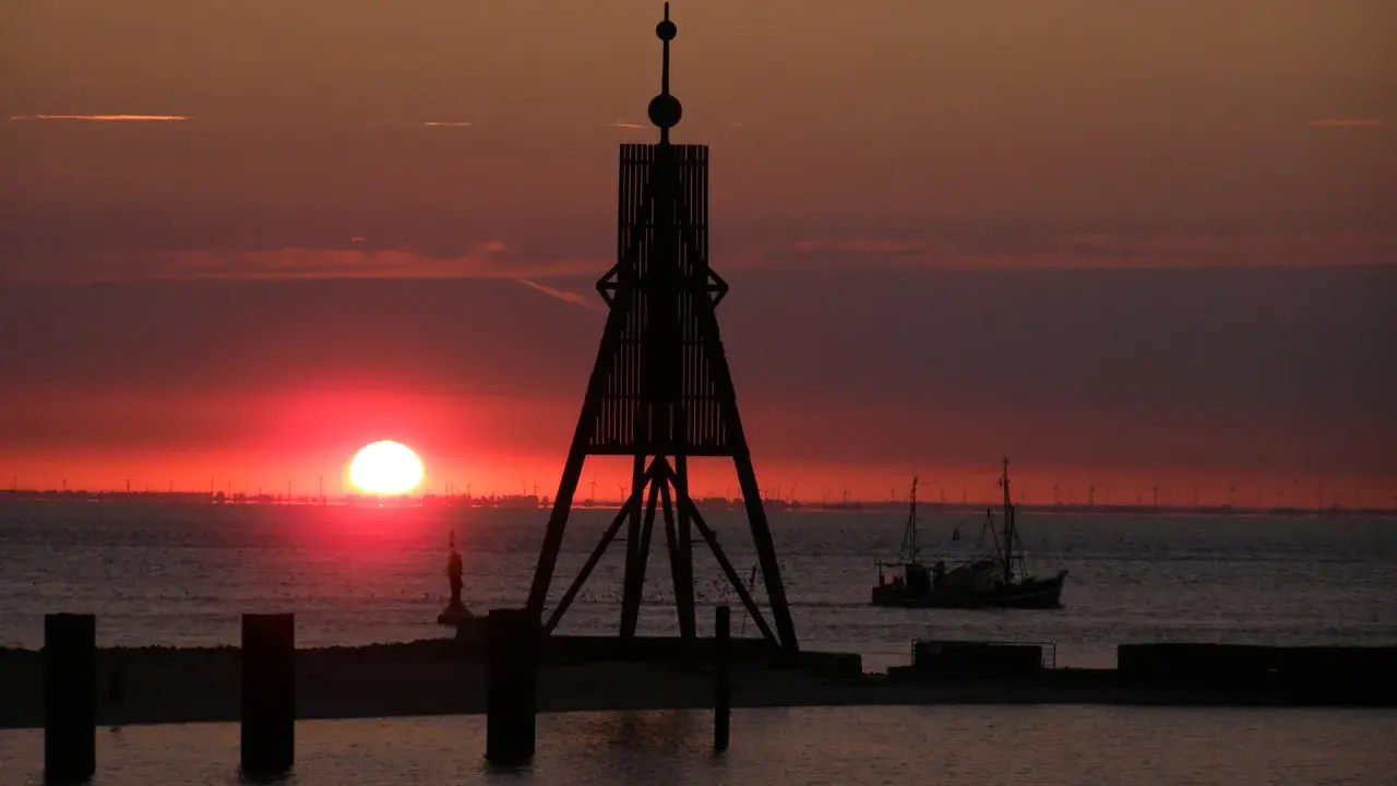 Sonnenuntergang in Cuxhaven: Ein Leuchtfeuer und ein Fischerboot auf dem Meer. Hier kann man die Weite genießen und den Tag ausklingen lassen.