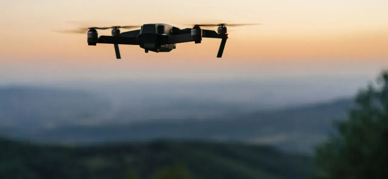 Czarny dron unosi się nad wzgórzami o zachodzie słońca.