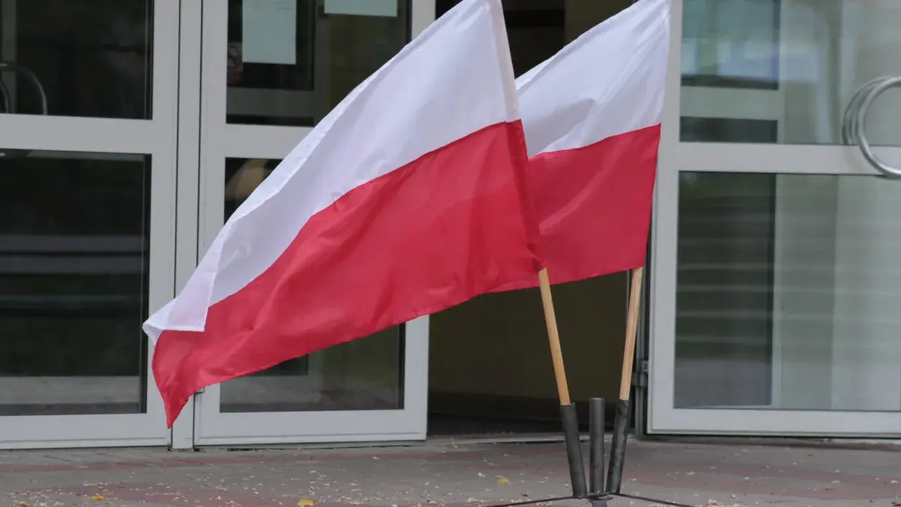 Dwa polskie flagi przed budynkiem. Dowiedz się, jak głosować za granicą, by Twój głos miał znaczenie.