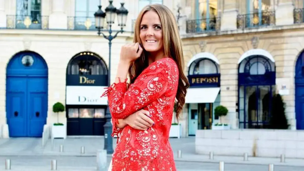 En kvinna i röd spetsklänning poserar framför Dior i Paris. Drömmer om ett jobb inom mode.