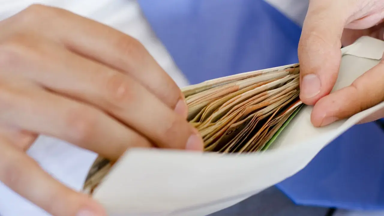 Dłonie wkładają plik banknotów do koperty na wesele.