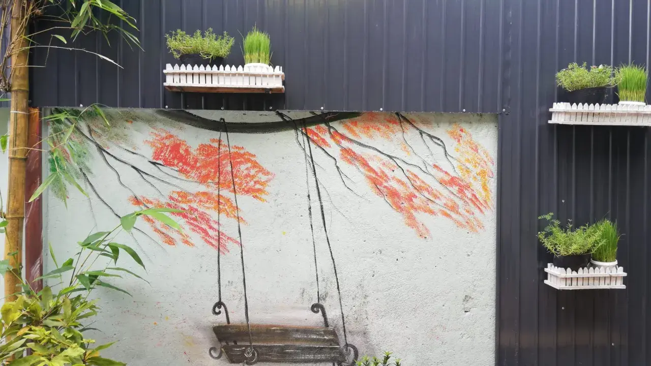 Un columpio pintado en un muro, ideal para inspirar al pintar patios pequeños. Las ramas anaranjadas y el bambú añaden color.
