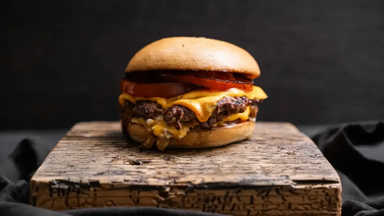 Saftiger Oklahoma Smash Burger mit geschmolzenem Käse und Tomaten auf rustikalem Holzbrett.