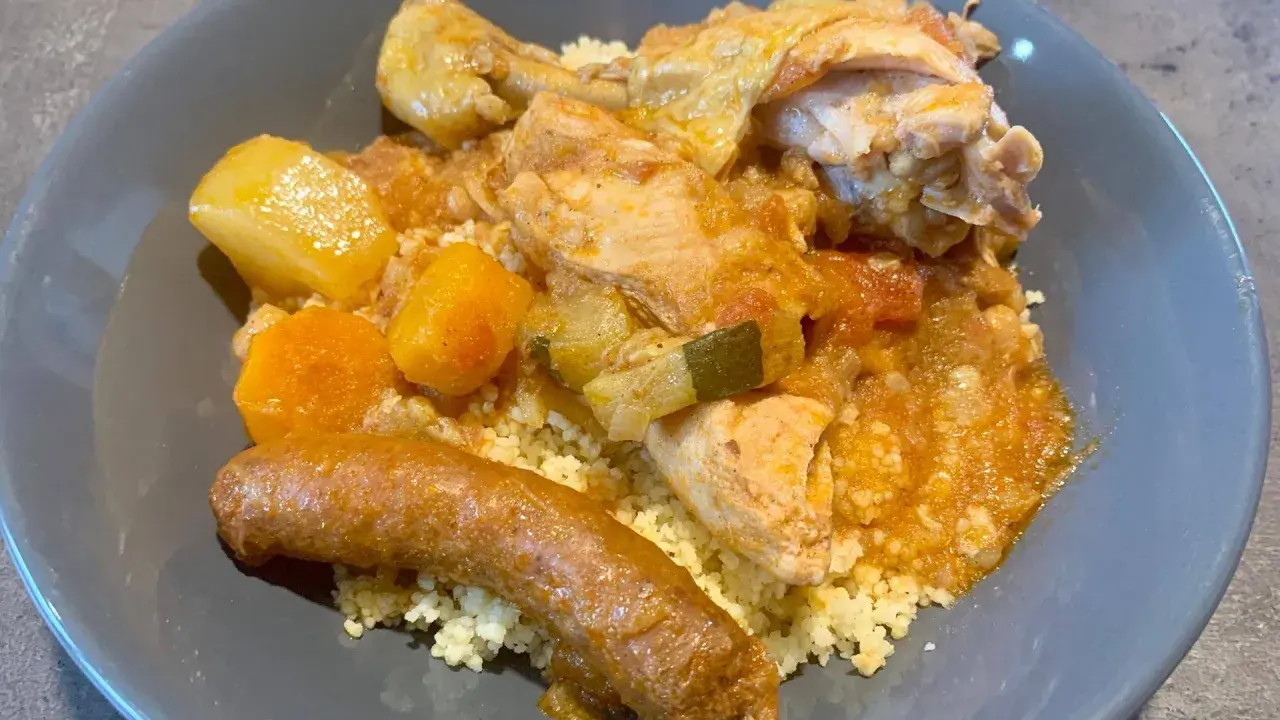Un plat appétissant de tajine poulet merguez, servi sur un lit de semoule, avec des morceaux de poulet, des légumes et une merguez dorée.