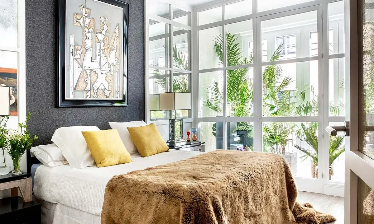 Un dormitorio moderno con cama mullida, arte abstracto y ventanales que invitan a diseña tu dormitorio con luz natural y plantas.