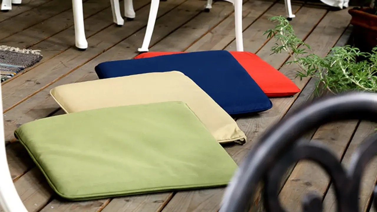 Mehrere bunte gartenpolster nass geworden, liegen auf einer Holzterrasse neben Gartenmöbeln.