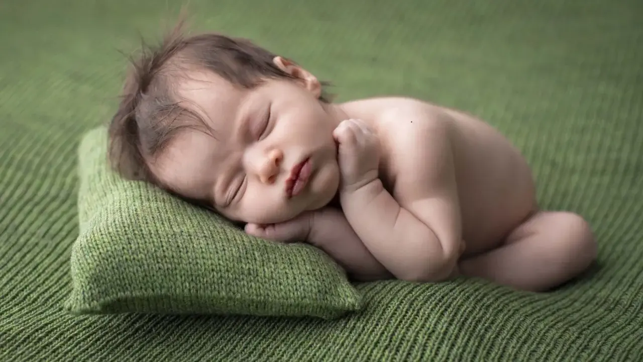 Dolce neonato scatti nel sonno, appoggiato su un cuscino verde. La sua manina è vicino al viso, in un sonno profondo e sereno.