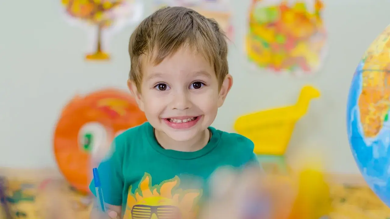 Niño sonriente con camiseta verde, rodeado de materiales educativos. Fomenta la autoestima en niños.