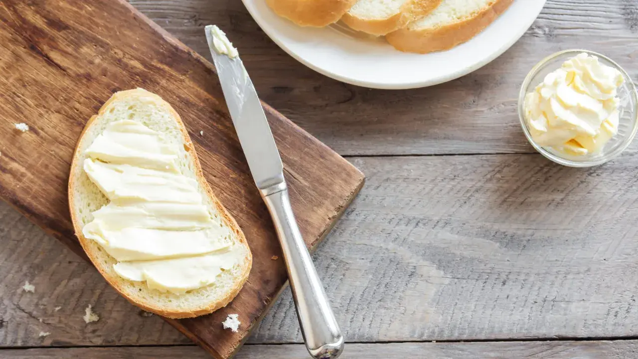 Brot mit Butter bestrichen, daneben eine Schale mit Butter und ein Messer. Ob Butter oder Margarine, beides enthält Cholesterin.