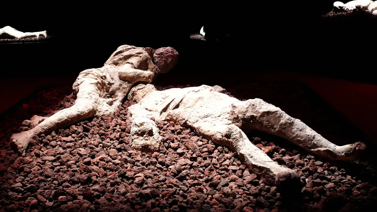 Pompeje zastygli ludzie w popiele, ostatnie chwile uwiecznione w kamieniu. Dwie postacie leżą obok siebie, otoczone gruzem.