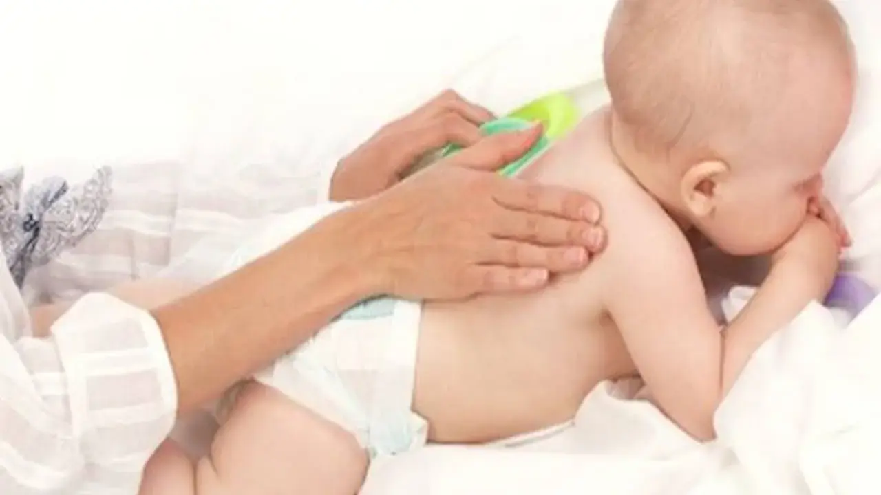 Delikatny masaż pleców niemowlaka, który waży już 9 kg. Ręce opiekuna głaszczą jego plecy.
