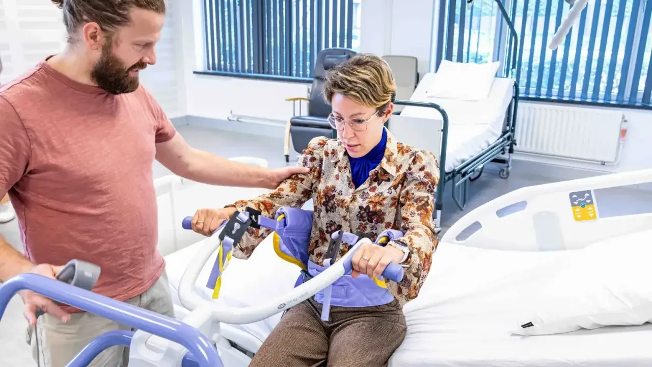 Un homme aide une femme à s'asseoir sur un lève-personne, illustrant l'ergonomie infirmier pour un transfert sécurisé.
