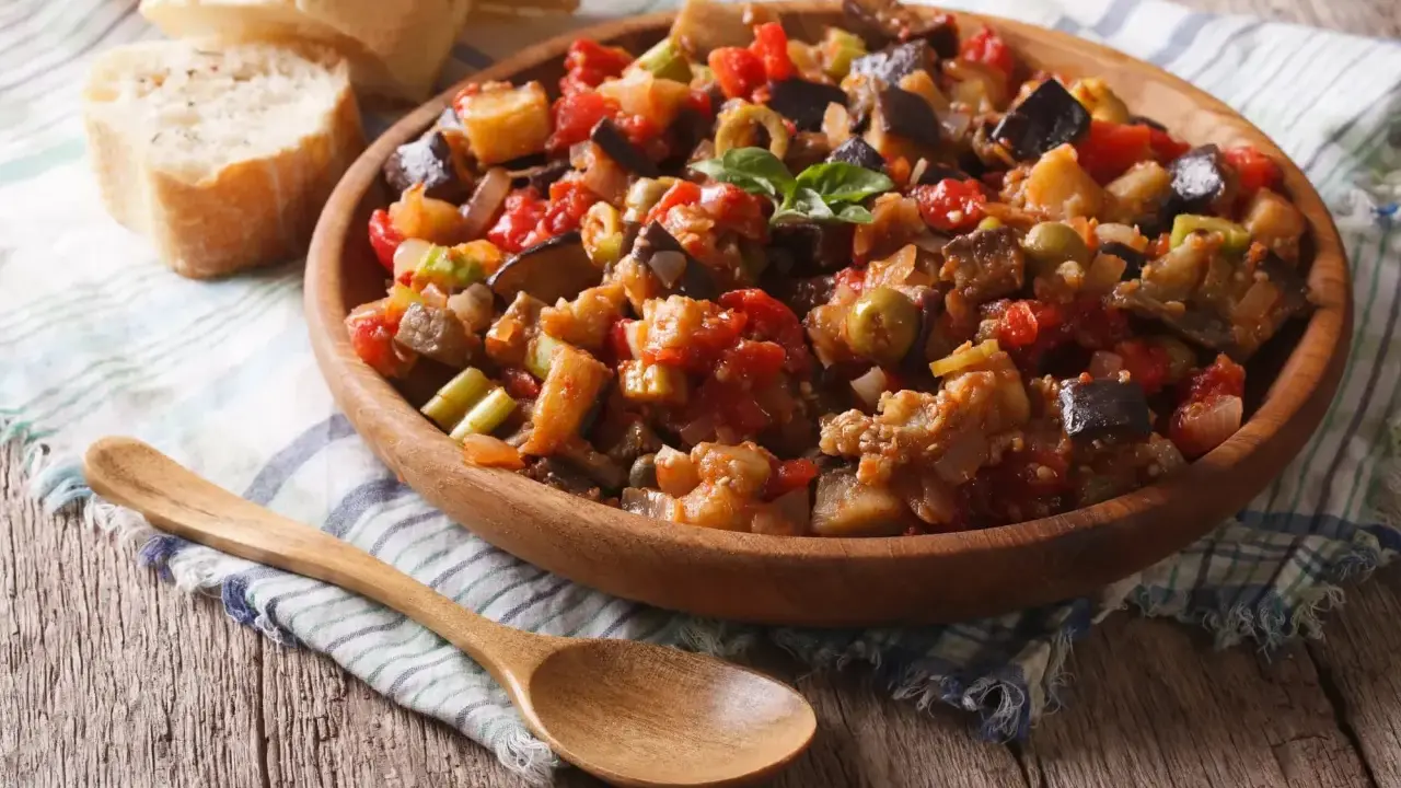 Un plat de caponata, une recette sicilienne savoureuse, garni de basilic frais, servi avec du pain croustillant.