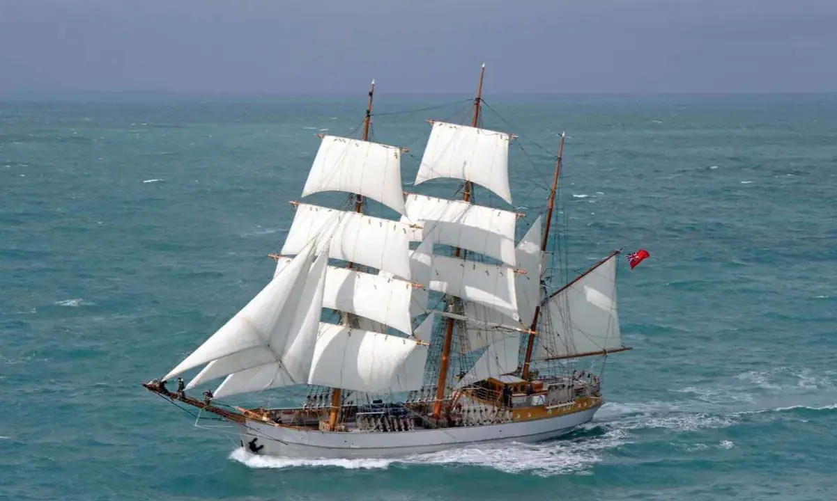 Majestueux voilier 3 mats, ses voiles blanches gonflées par le vent, navigue sur une mer agitée.