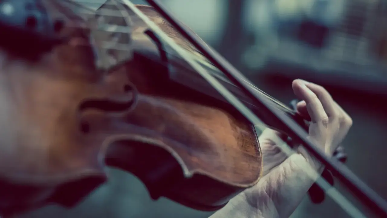 Main d'un musicien jouant du violon, un instrument à cordes, pas à vent. La musique s'élève.