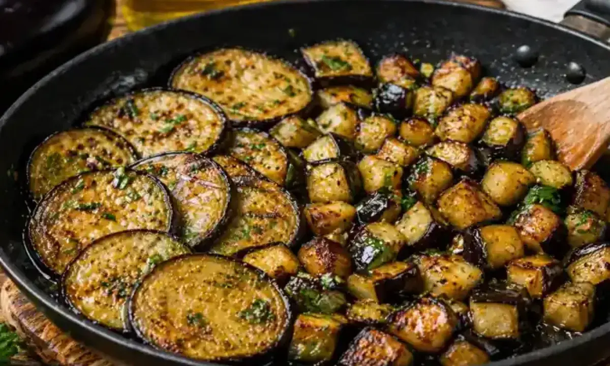 Aubergines sautées dans une poêle, certaines en rondelles, d'autres en dés, parsemées d'herbes fraîches. Un délice à déguster !